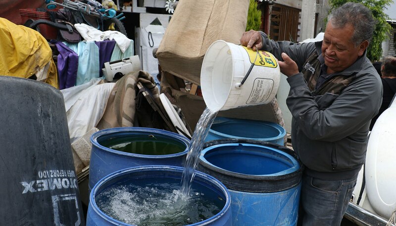Un hombre vierte agua de un balde a un barril.