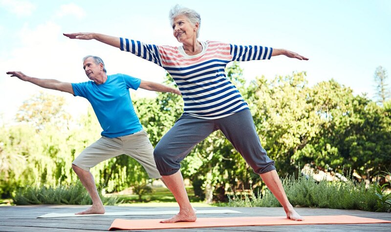 Pareja de ancianos haciendo yoga al aire libre