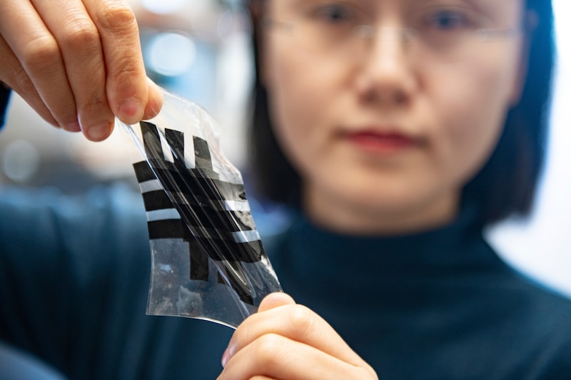 Científica sosteniendo una hoja de material transparente con un patrón de líneas negras.