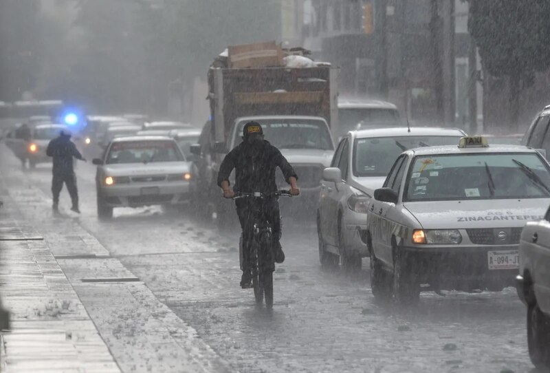 Titulo: Ciclista intrépido desafía la lluvia en medio del tráfico de la ciudad