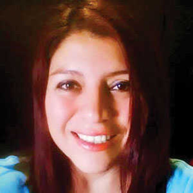Mujer joven con pelo rojo y ojos marrones sonríe.