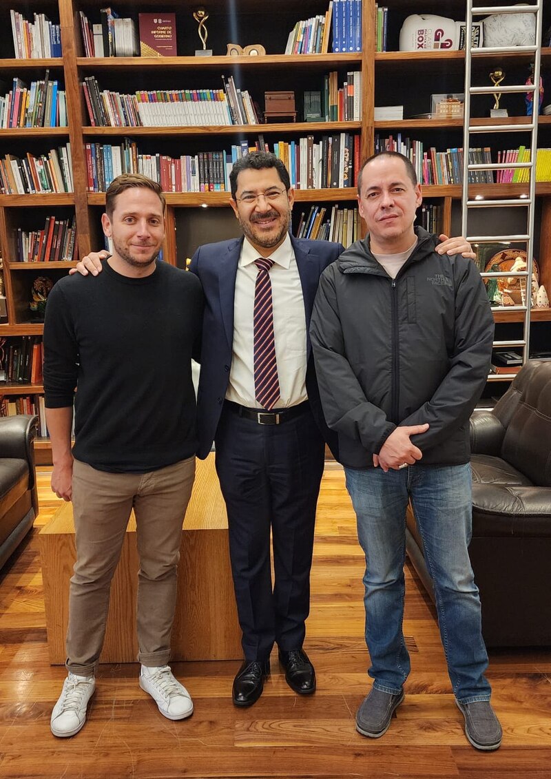 Tres hombres sonríen y posan para una foto en una biblioteca.