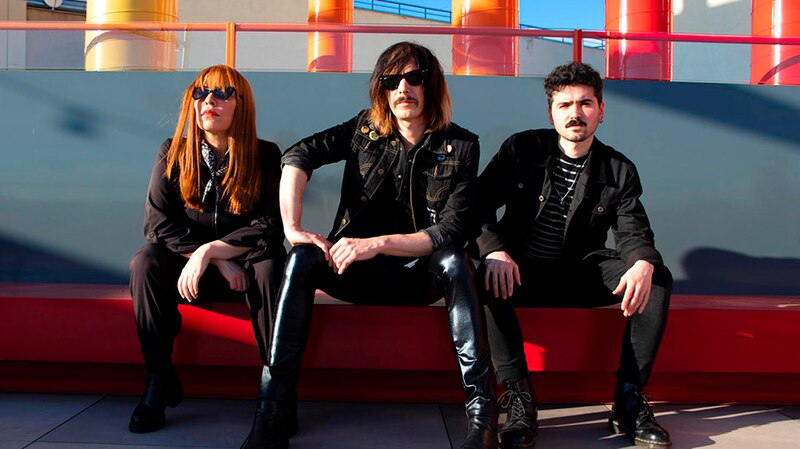 Tres personas con gafas de sol sentadas en un banco rojo