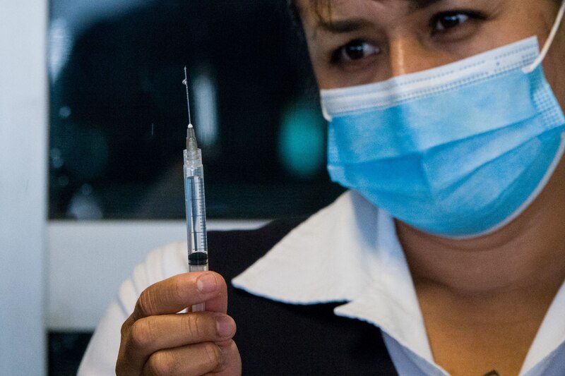 Mujer con mascarilla sosteniendo una jeringa