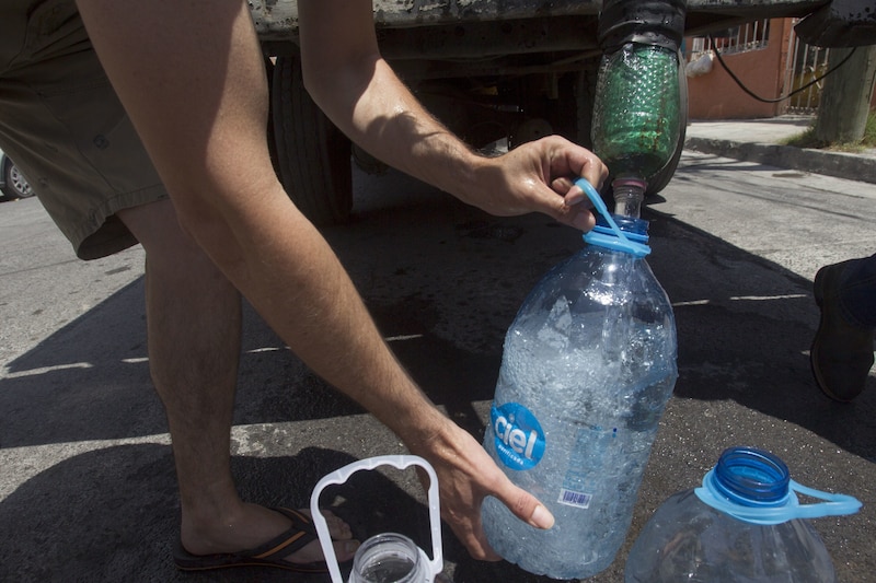 Un hombre llena una botella de agua helada en una calle de Caracas