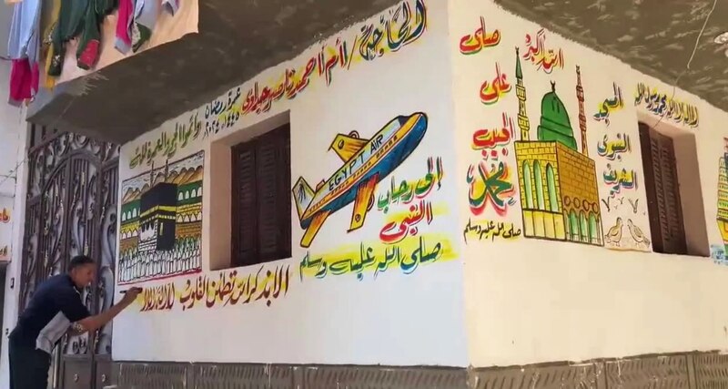 Un hombre pinta un mural en una pared en el que se puede ver una mezquita, un avión y la Kaaba