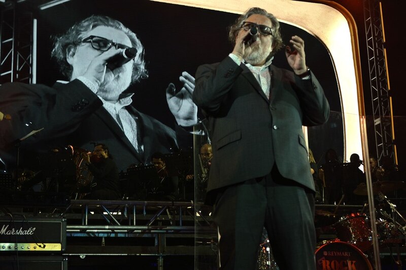 Un cantante actúa en un concierto con una pantalla gigante detrás de él que muestra su imagen en blanco y negro.
