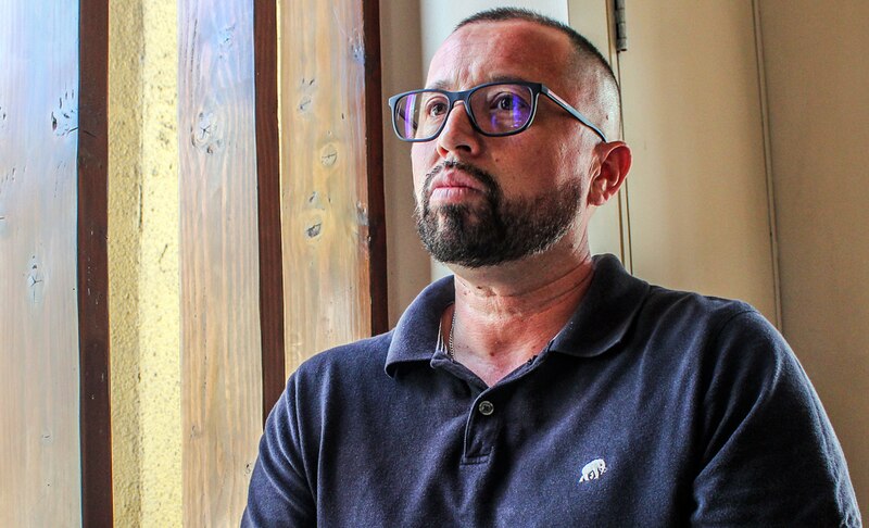 Un hombre con barba y lentes mira por la ventana