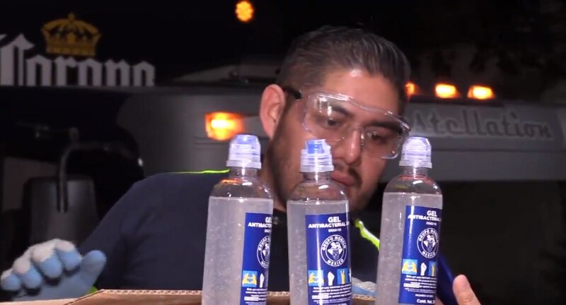 Un hombre con gafas de seguridad y guantes vierte gel antibacterial en botellas.