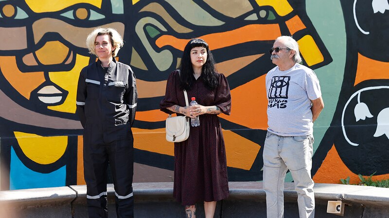 Tres personas de pie frente a un mural