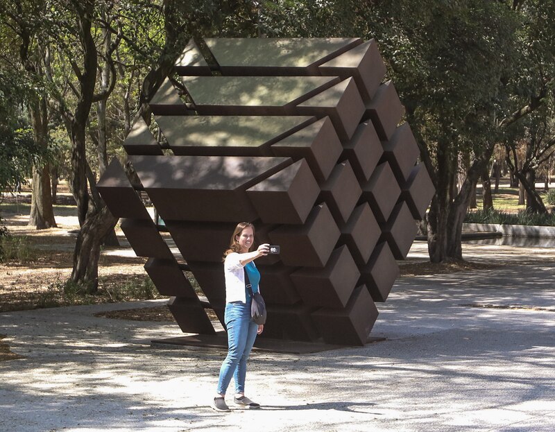 Mujer tomando una foto de una escultura de metal en un parque