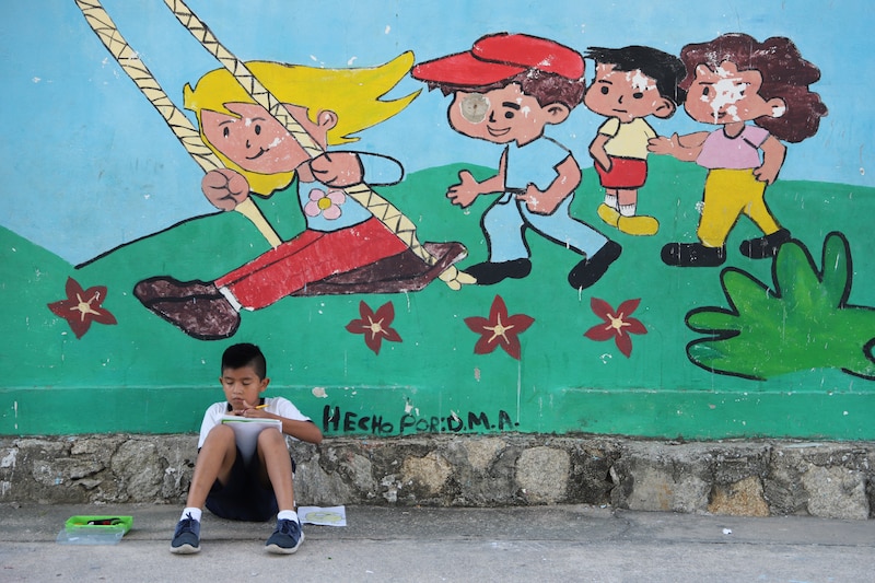 Niño hondureño sentado junto a un mural