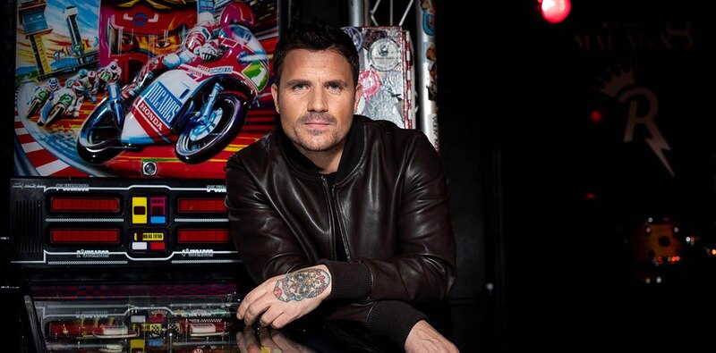 El cantante Robbie Williams posa junto a una máquina de pinball.