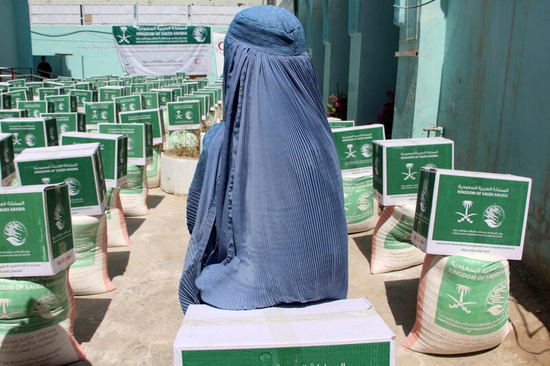 Mujer afgana con burka sentada junto a cajas de ayuda humanitaria
