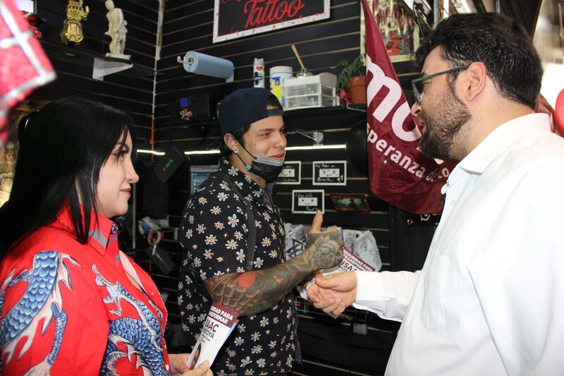 Un político saluda a una pareja en un puesto de tatuajes.