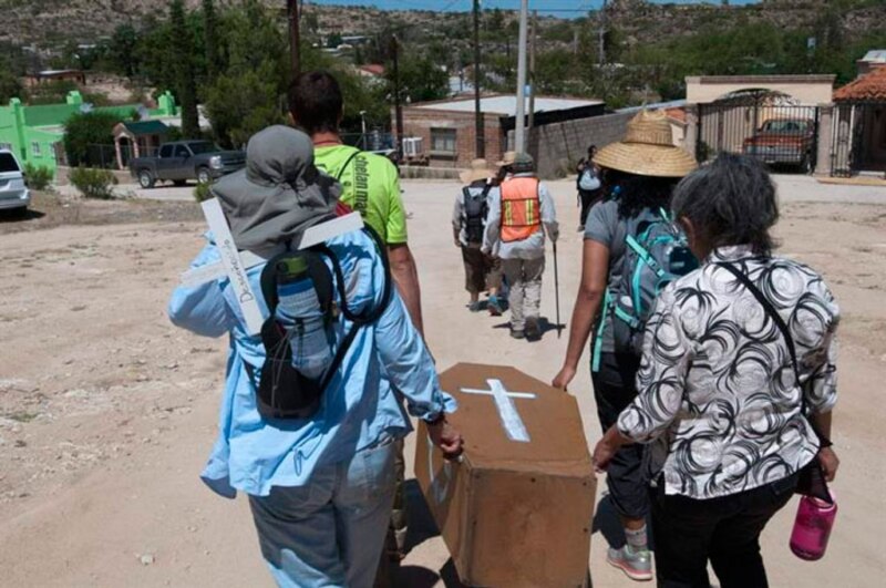 Un grupo de personas cargando un ataúd en un camino rural.