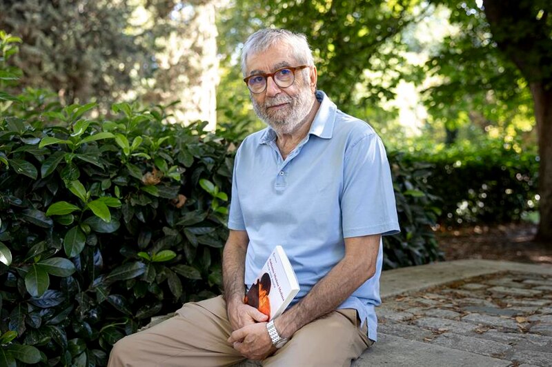 El escritor Arturo Pérez-Reverte, sentado en un banco y leyendo un libro.