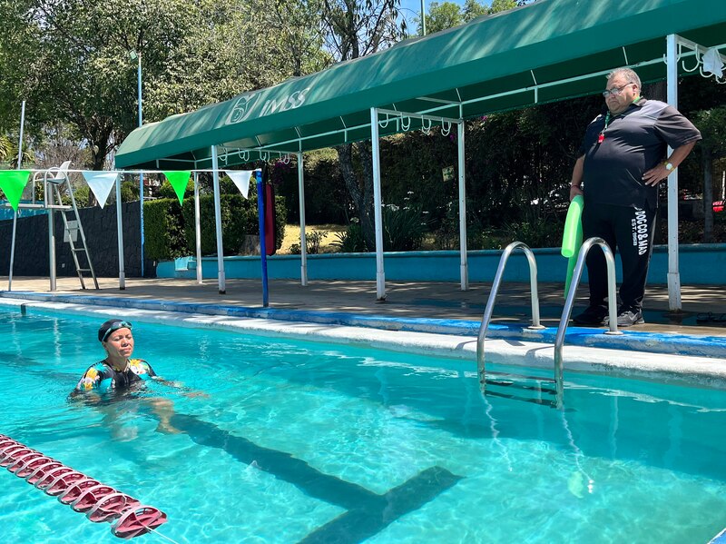 Mujer nada en la piscina mientras un hombre la observa