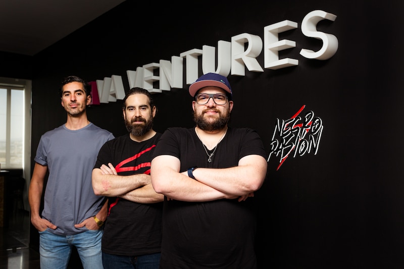 Tres emprendedores sonríen frente a un logo de fondo