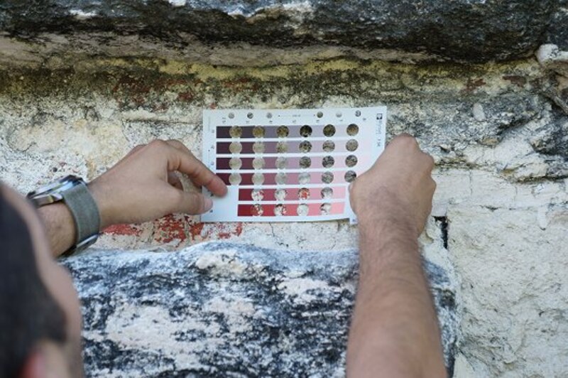 Un arqueólogo utiliza una carta de colores para comparar los colores de una pintura mural con los de la carta.