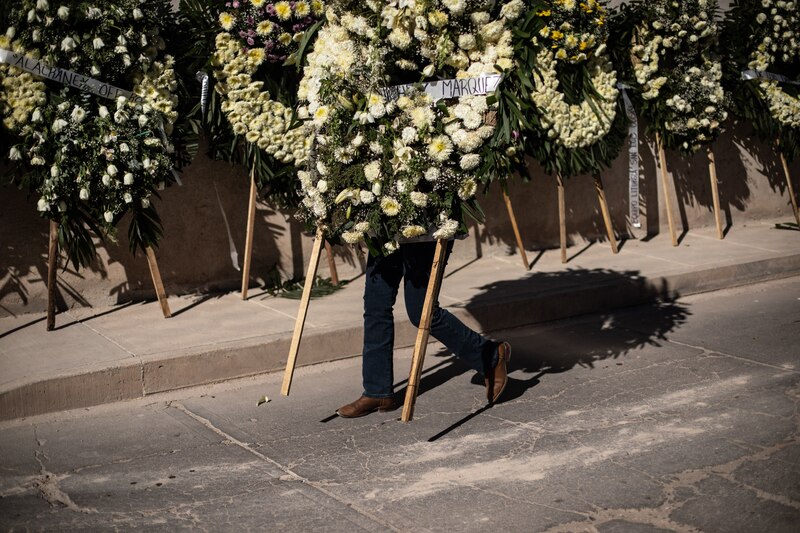 Un hombre camina cargando una corona de flores