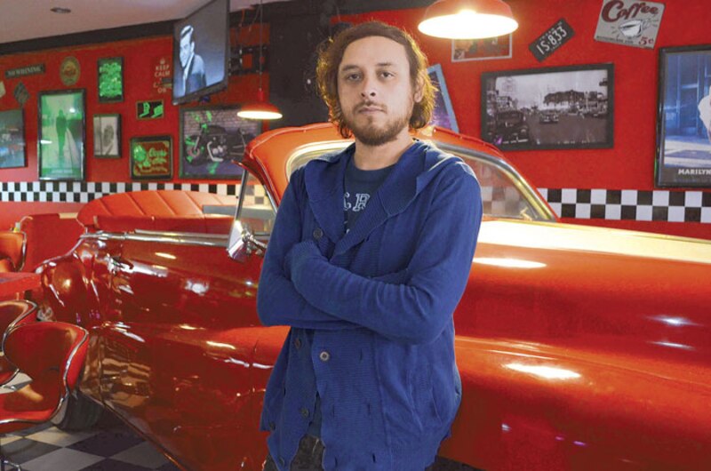 Un hombre posa junto a un auto rojo antiguo en un restaurante