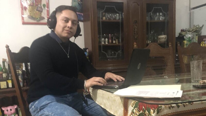 Un joven sentado en una mesa con un computador portátil.