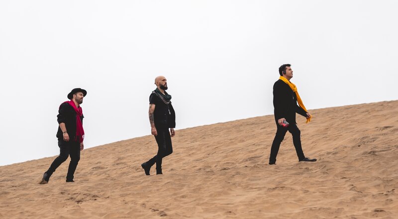 Tres hombres caminando por una duna de arena en el desierto