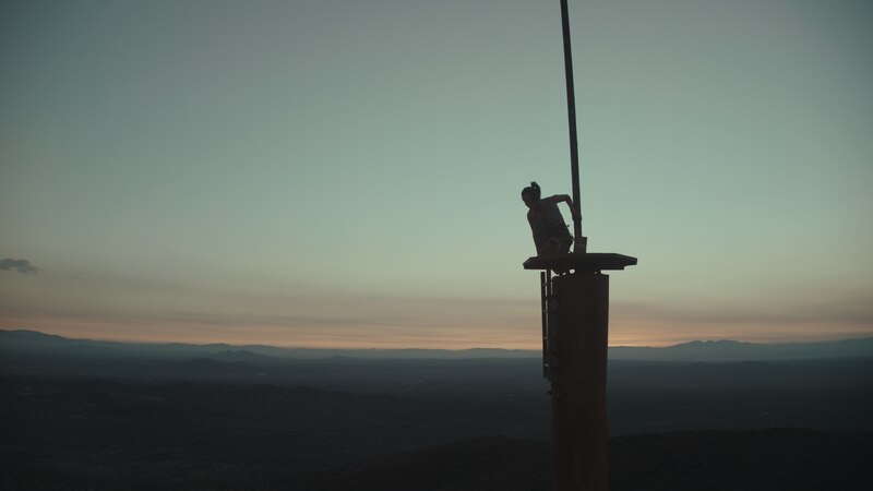 Silueta de un hombre en la cima de una torre de telecomunicaciones al atardecer