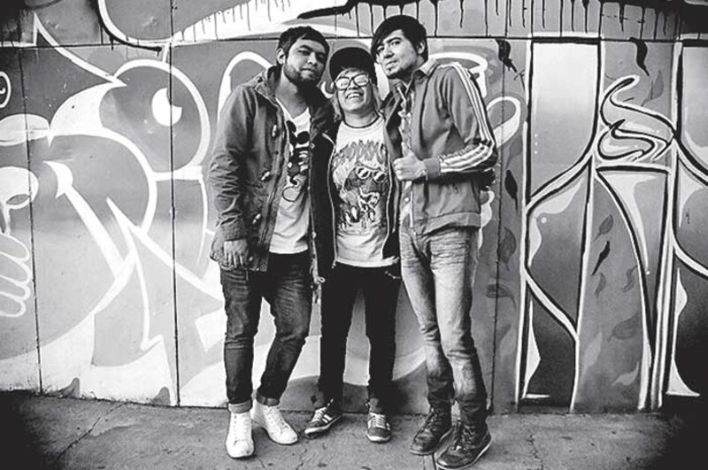 Tres hombres sonríen frente a un mural