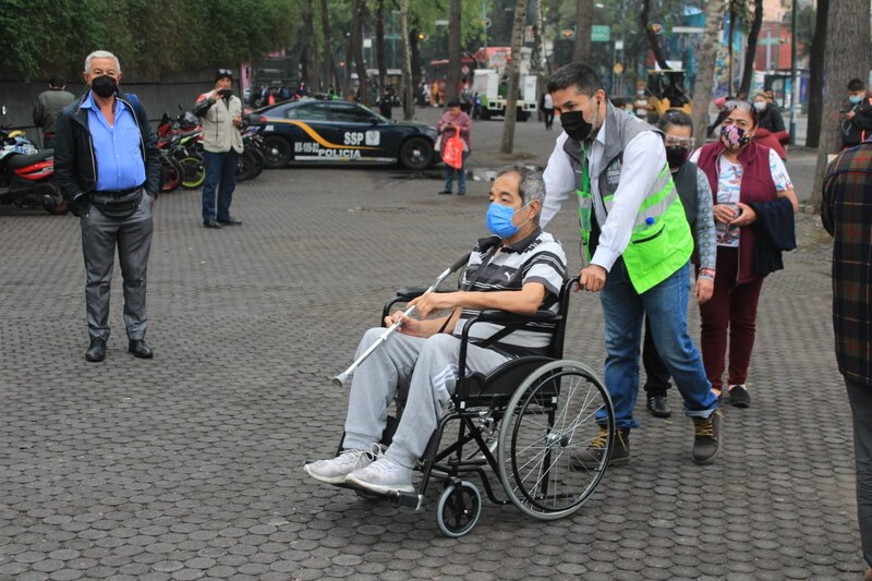 Un hombre en silla de ruedas es empujado por un voluntario en un parque.