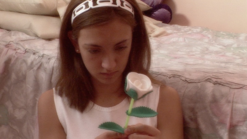 Una jovencita sostiene una rosa blanca