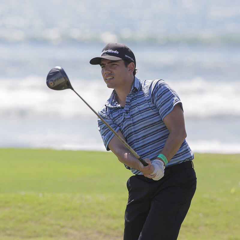 Golfista masculino joven jugando un tiro de golf en un campo de golf con el mar de fondo