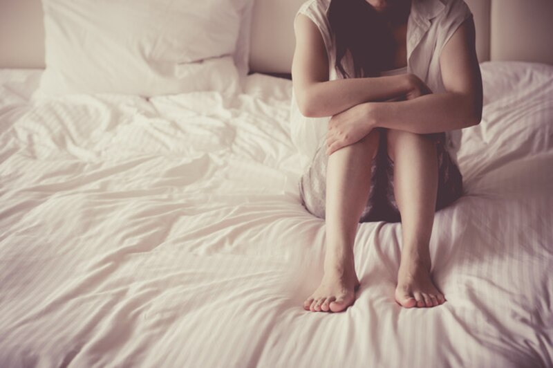 Mujer sentada en la cama con los brazos alrededor de las piernas