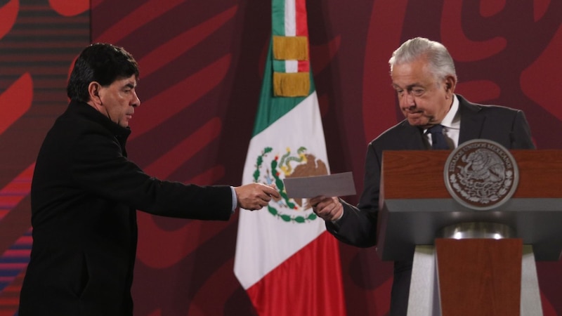 El presidente López Obrador recibe un documento de manos de un hombre durante una ceremonia oficial.