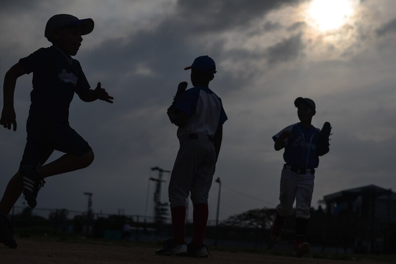 Siluetas de niños jugando béisbol al atardecer