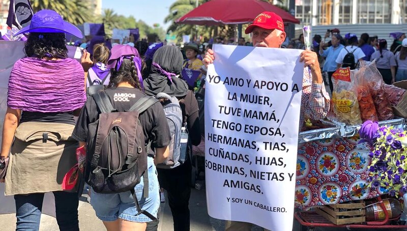 Title: Un hombre sostiene un cartel en una manifestación en apoyo a las mujeres