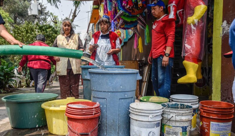 Personas en una comunidad se abastecen de agua de una manguera