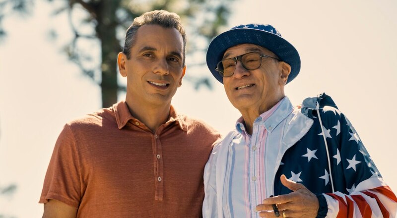 Dos hombres sonrientes, uno de ellos con una bandera de los Estados Unidos.