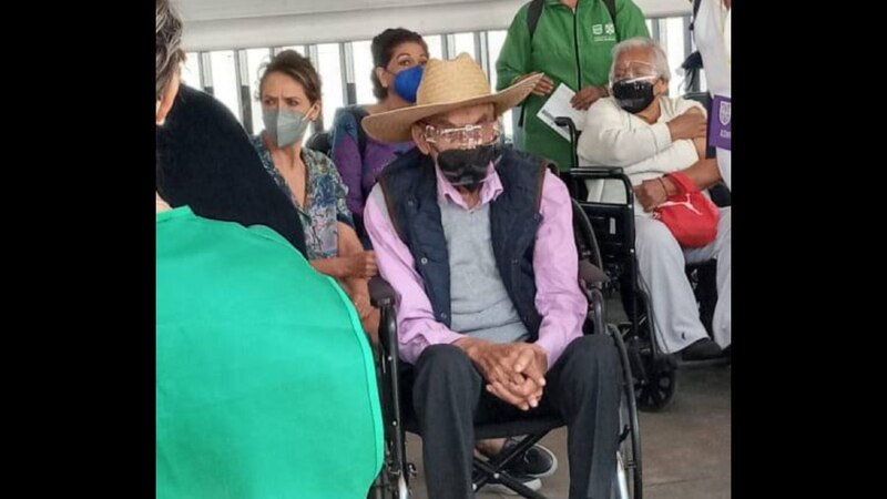 Un anciano en silla de ruedas observa a los trabajadores de la salud que aplican vacunas contra el COVID-19.