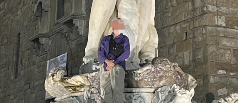 Un hombre se encuentra de pie sobre una estatua de un león en Florencia, Italia.