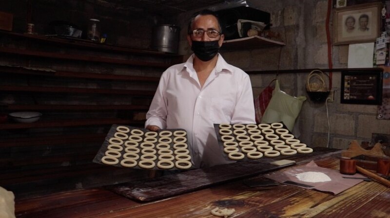 Un panadero sostiene dos bandejas de galletas en una panadería.