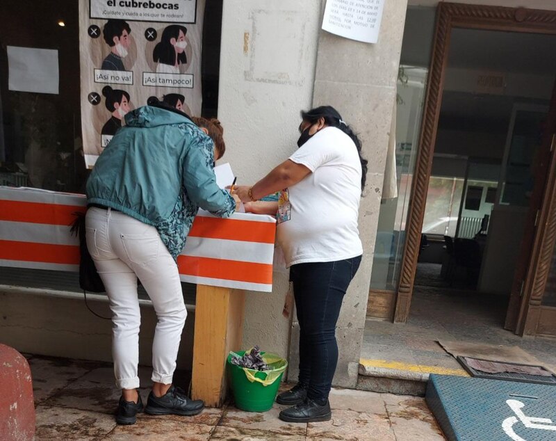 Mujeres firman en una mesa con una bandera de México.