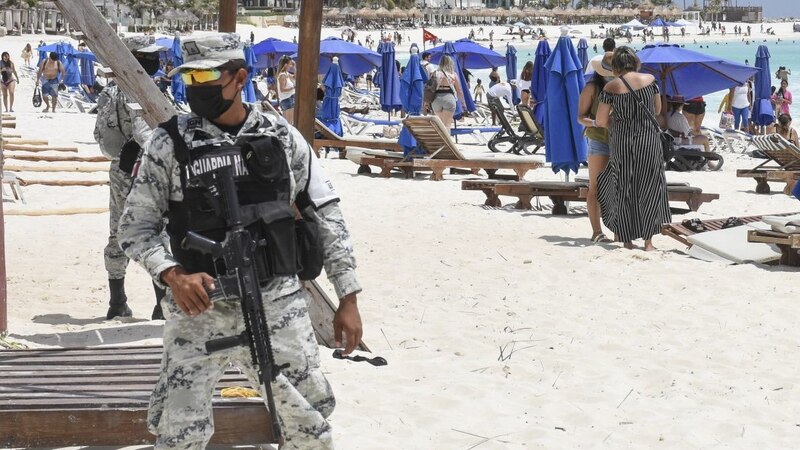 Playa en Cancún con turistas y un soldado de la Guardia Nacional