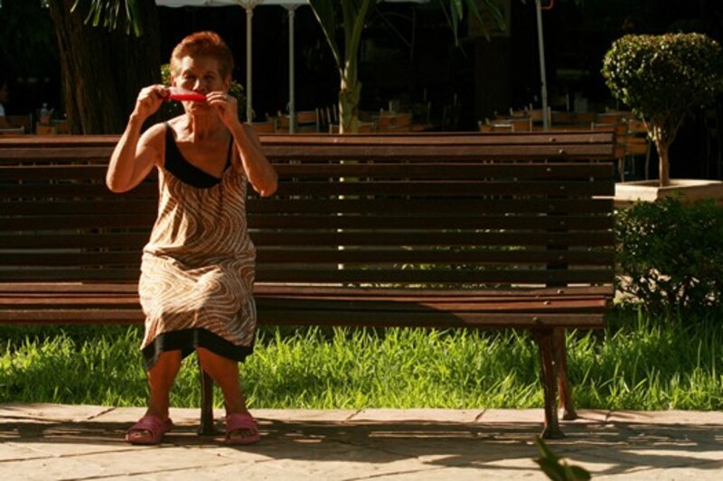 Mujer mayor comiendo una paleta de hielo en una banca del parque