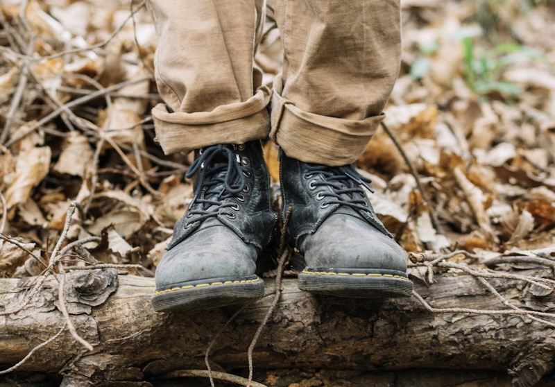 Pies con botas Dr. Martens sobre un tronco en el bosque