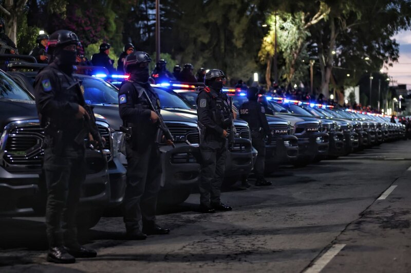 Policías fuertemente armados custodian camionetas policiales en una calle oscura