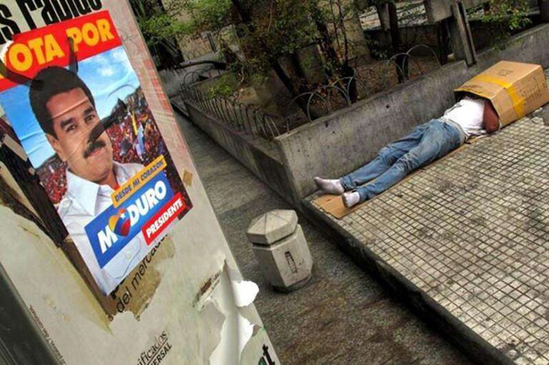 Un hombre sin hogar duerme en la calle junto a un cartel político.