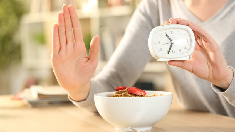 Mujer joven desayunando y mirando el reloj