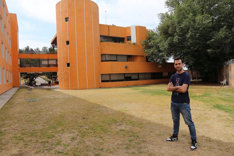 Un hombre joven parado frente a un edificio naranja